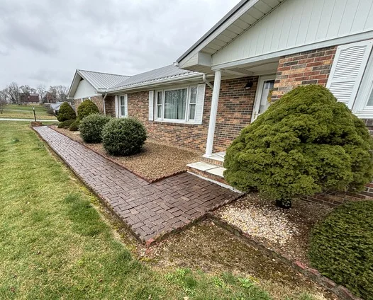 Red brick walkway leading to brick home entrance with freshly mulched beds, perfectly manicured round evergreen shrubs, and professional landscape installation