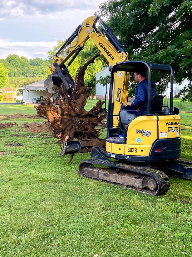 A professional using an excavator equipment to grind and remove stump on a residential yard