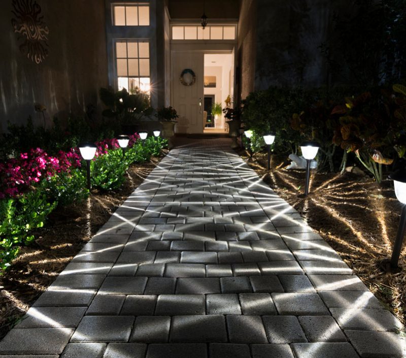 A brick walkway illuminated by solar-powered lights at night.